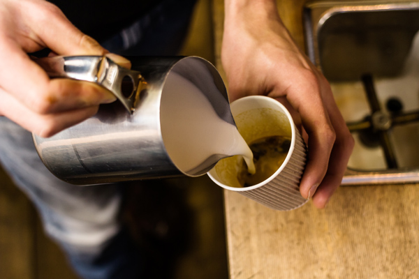 hot milk being poured by barista into cardboard takeaway coffee cup